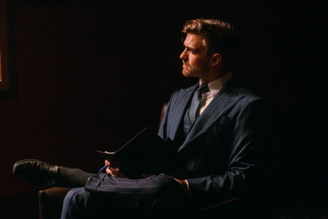 a man in a Formal Wear Tailoring Suit sitting in a dark room
